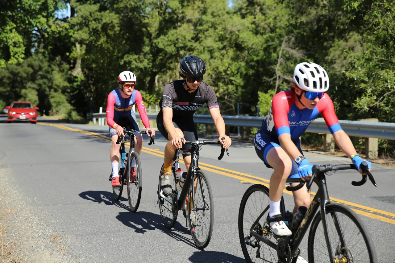 Three junior cyclists ride together on a wooded road
