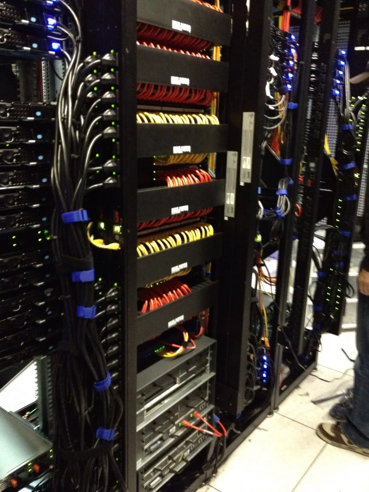 The back of the racks after cabling: bundled red and yellow network cables, blue velcro ties and power cords, with status lights on